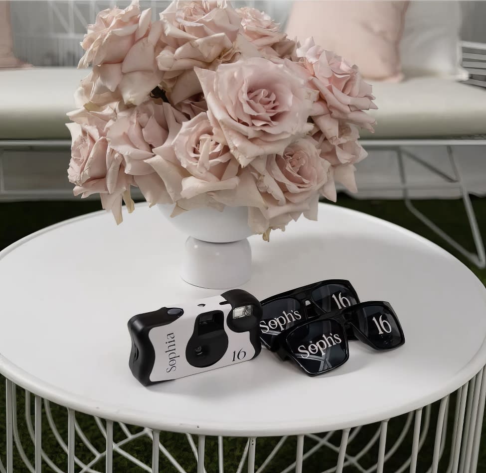 A white wire coffee table with a camera and a vase of roses.