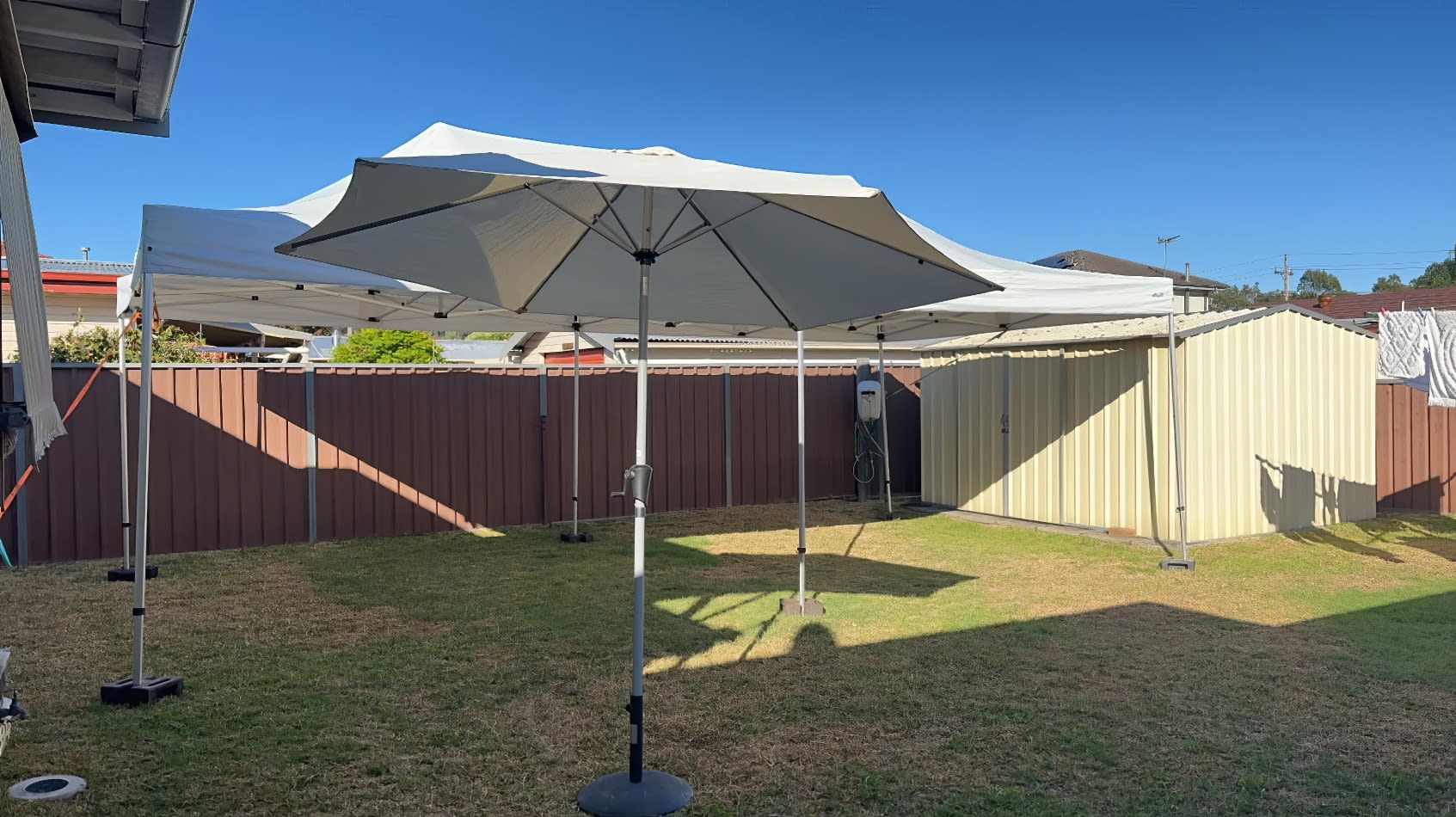 A backyard with a white market umbrella and chairs.