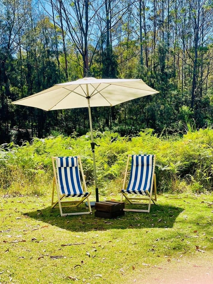 Two chairs shaded by a market umbrella in a grassy area.