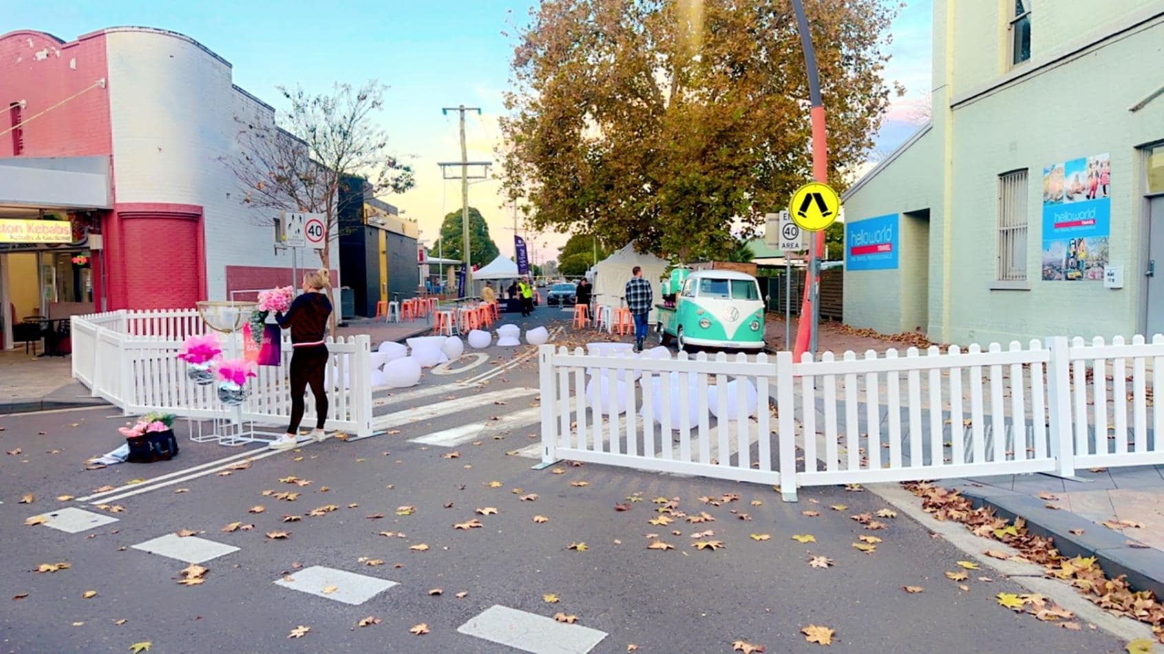 A street with a white picket fence and pink balloons.