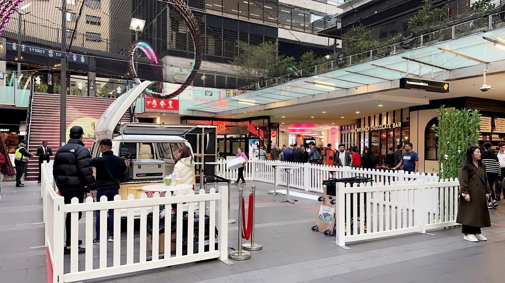 A white picket fence enclosing a bustling shopping mall.