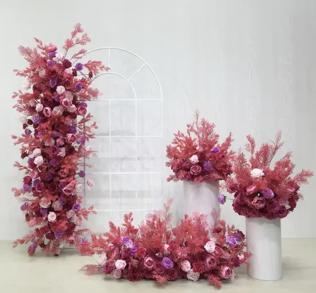 A bunch of pink flowers in vases on a table, beautifully adorned with white French window arch frame hire.