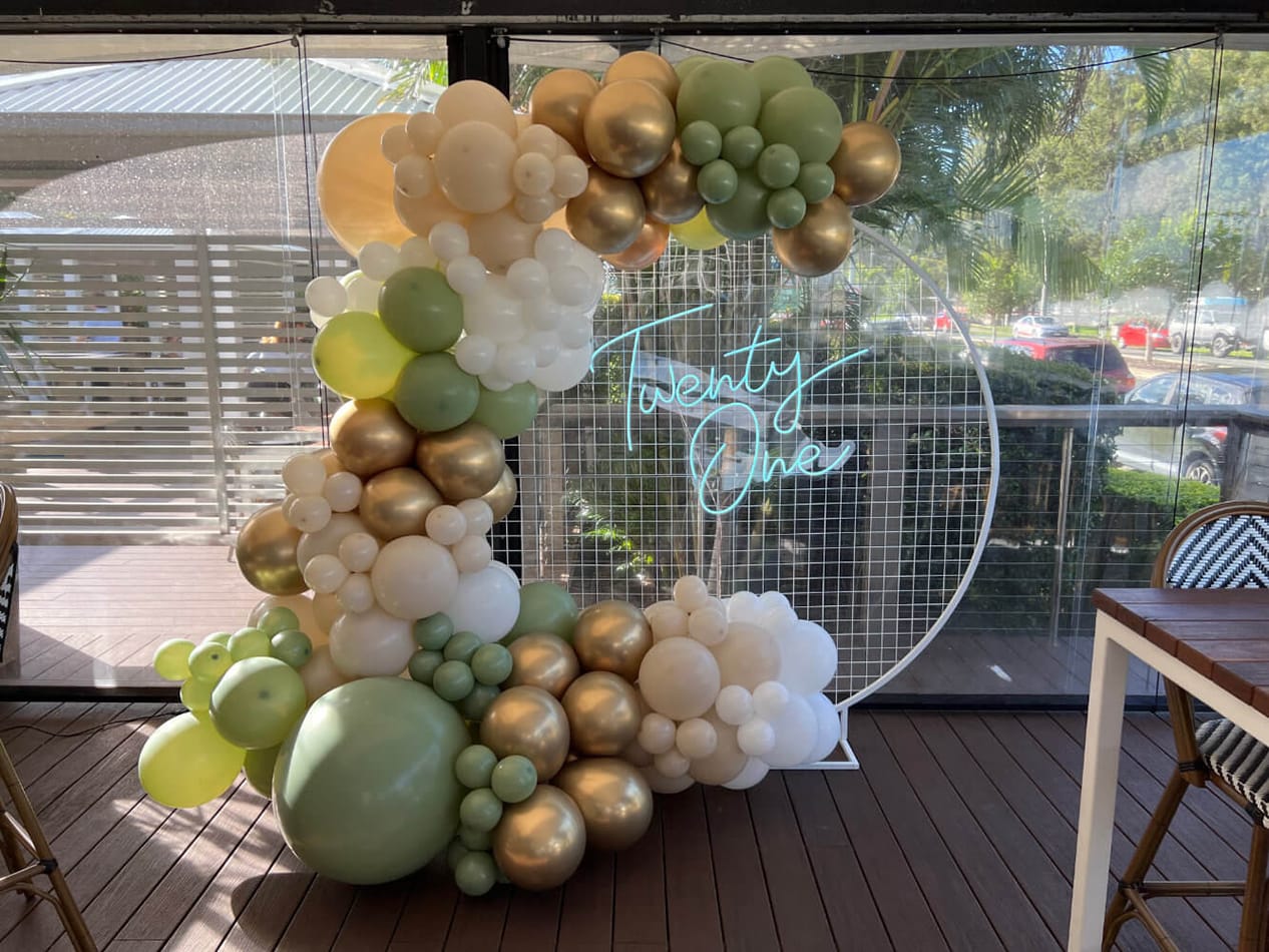 A balloon arch decorated with gold and green balloons for hire.