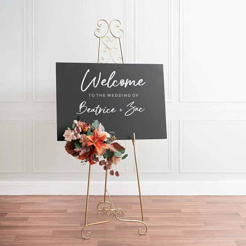 A welcome sign on a gold French easel adorned with flowers.