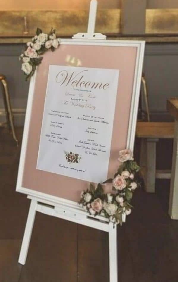 A white wooden easel hire with a welcome sign adorned by flowers