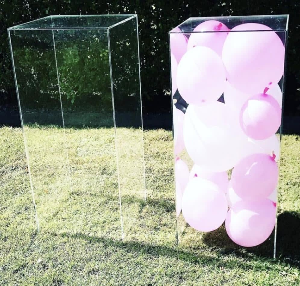 A clear square box with pink balloons in it.