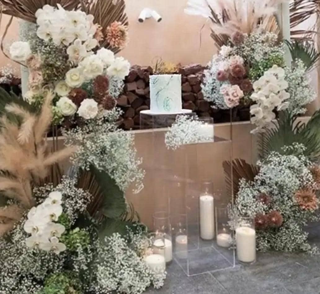 A wedding cake decorated with flowers, candles, and a clear square acrylic plinth.