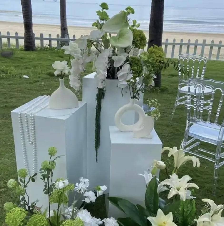 A large white flower arrangement on a table in front of a beach.