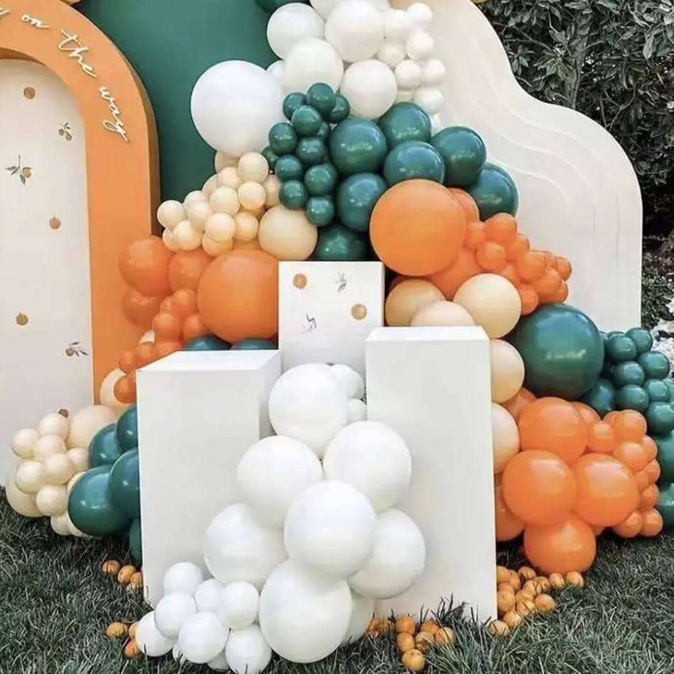 An orange and white balloon arch with green and white balloons, displayed on three white square plinths.