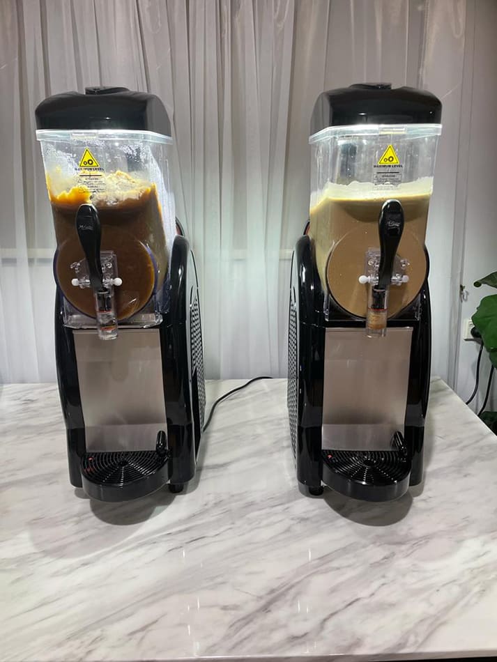 Slushie Machine Hire: Pkg 1 - Two ice cream machines on a marble counter serving up to *60 drinks*.