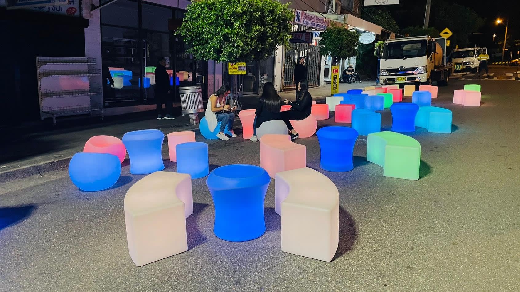 A group of colorful stools on a street at night, illuminated like a Glow Bench.