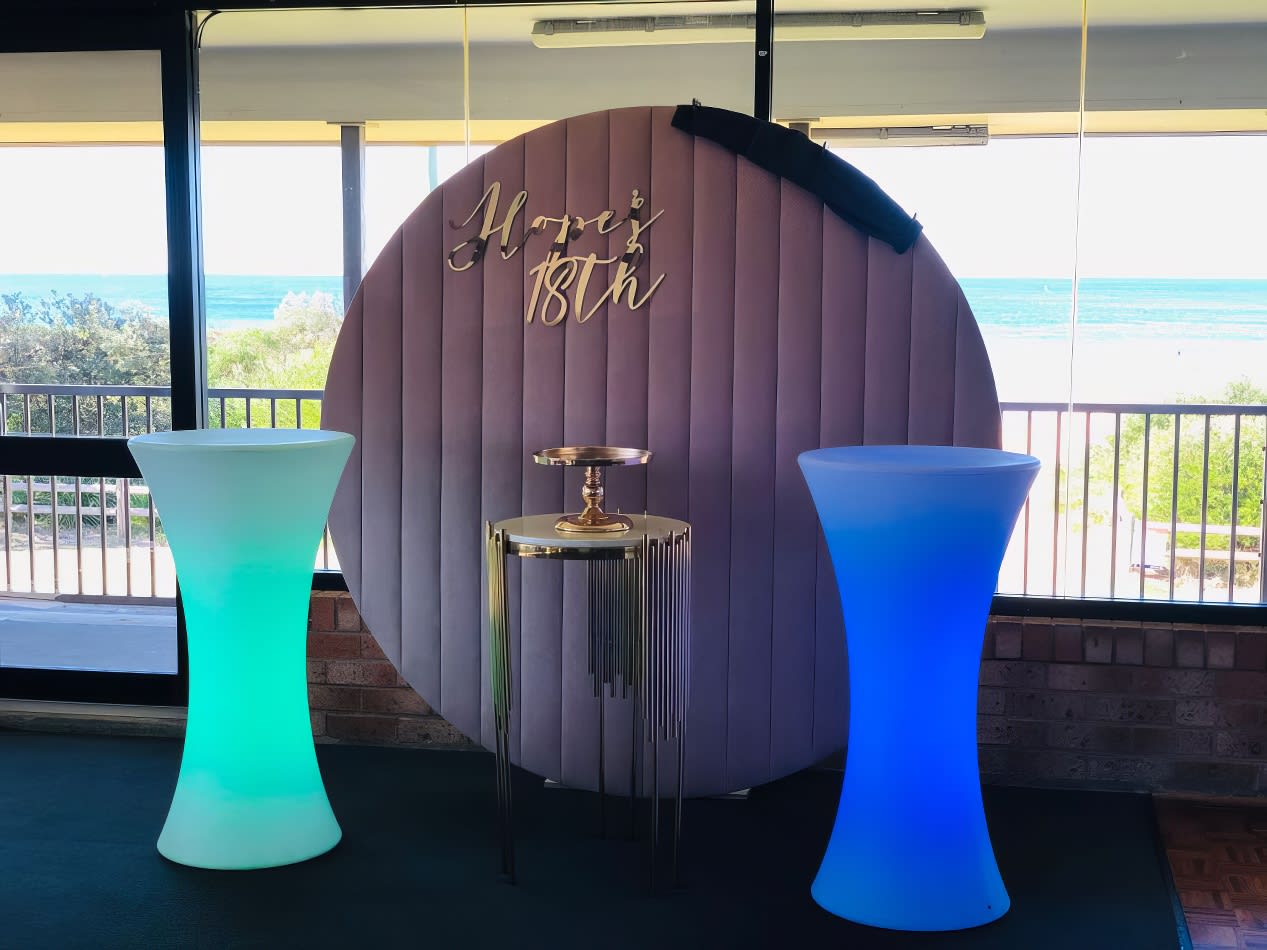 A glow cocktail bar table hire set up in front of a window, featuring a photo booth.