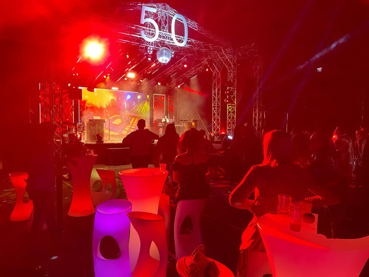 A group of people enjoying themselves at a concert, gathered around the Glow Cocktail Bar Table Hire.