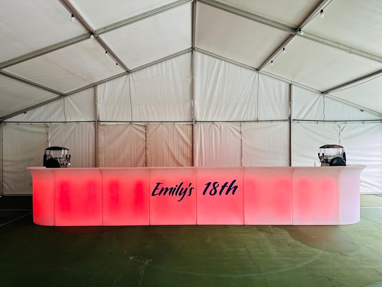 A large tent with a bar in the middle of it, featuring a dazzling Glow Corner Bar.