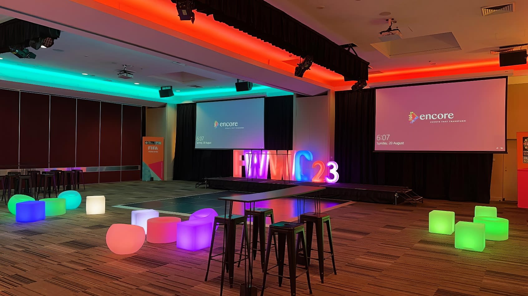 A conference room with colorful stools, a projection screen, and Glow Cube Hire for added vibrancy.