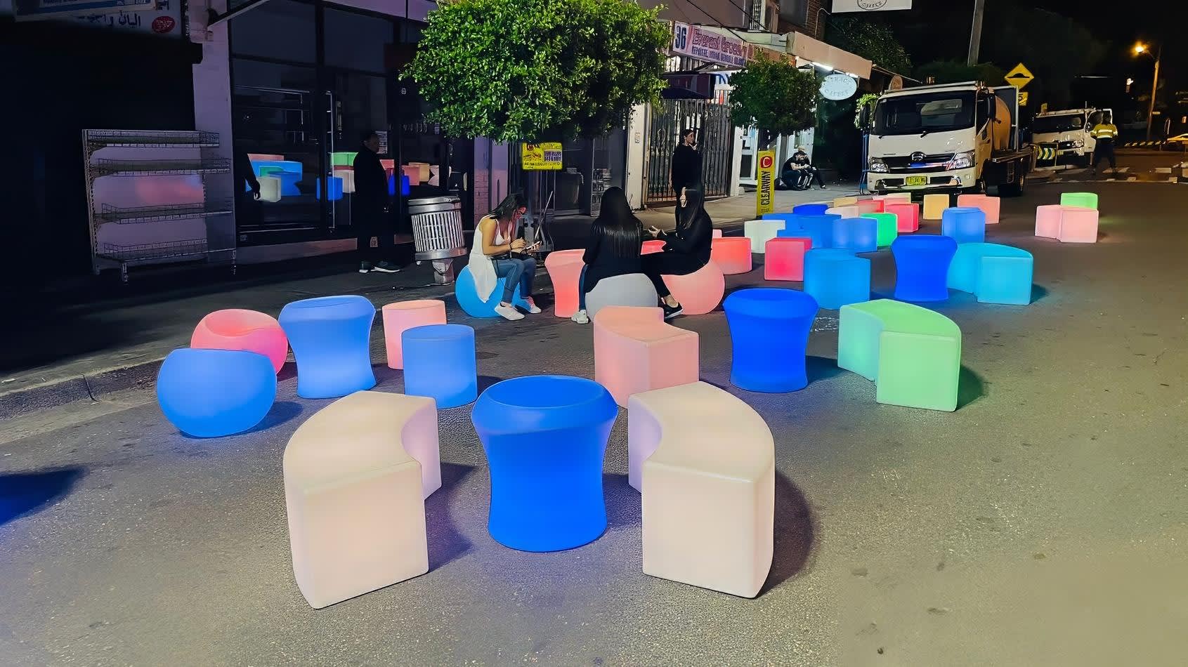 A group of colorful Glow Sphere chairs on a street at night.