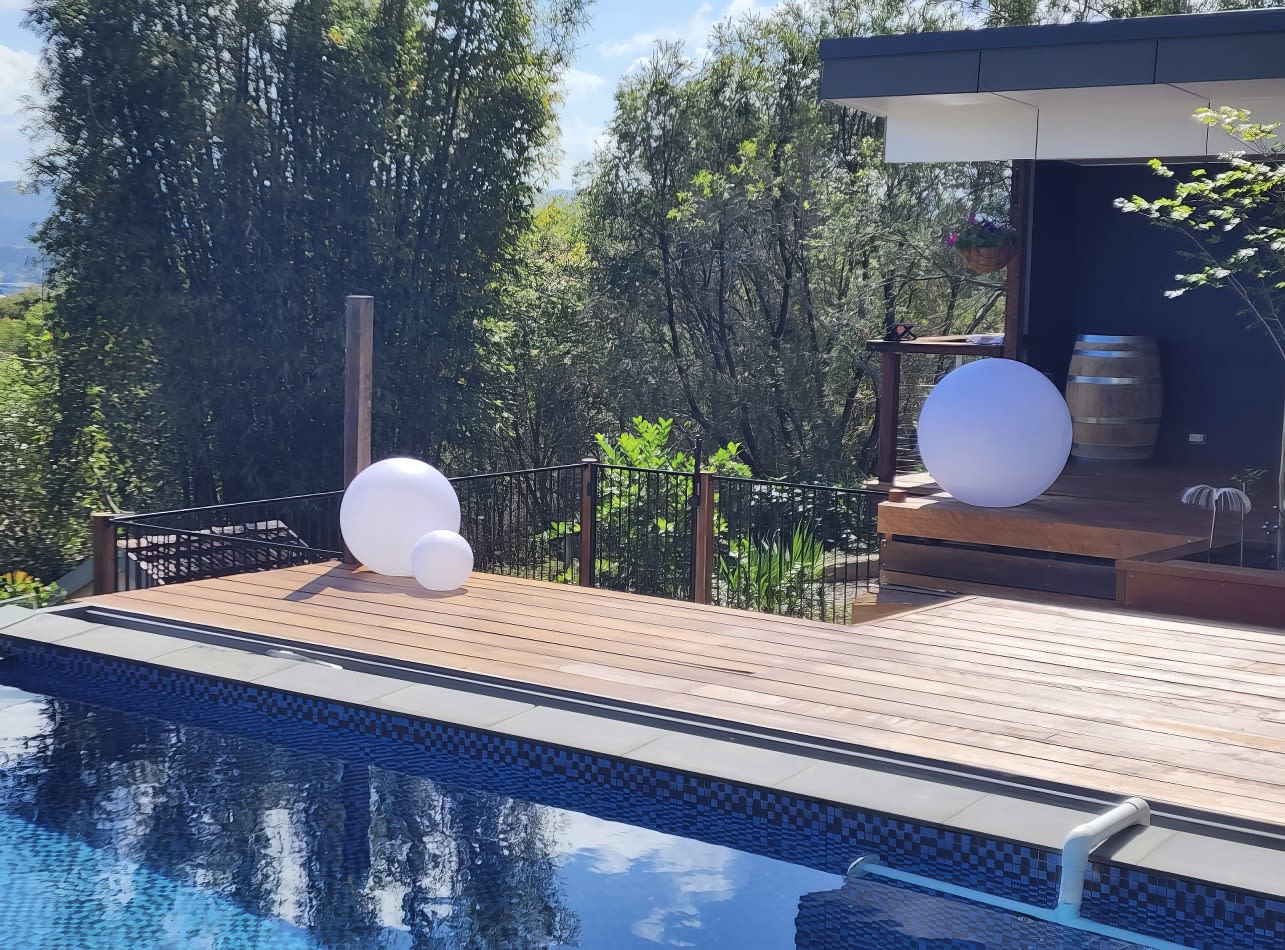 A wooden deck with a pool in the background, enhanced by the mesmerizing Glow Sphere Hire - 40cm.