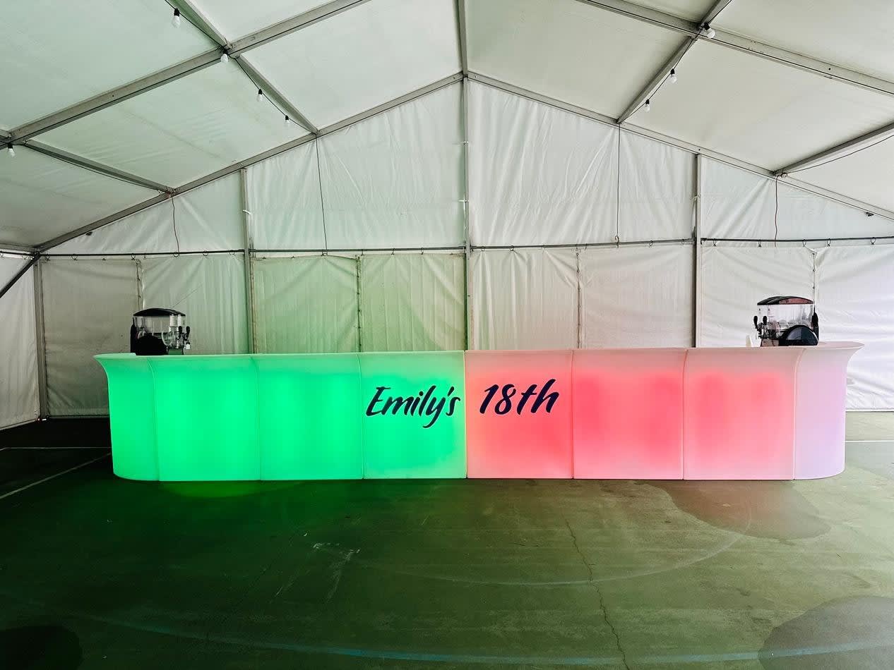 A straight LED bar in a tent, emitting a vibrant display of green, red, and blue glow.