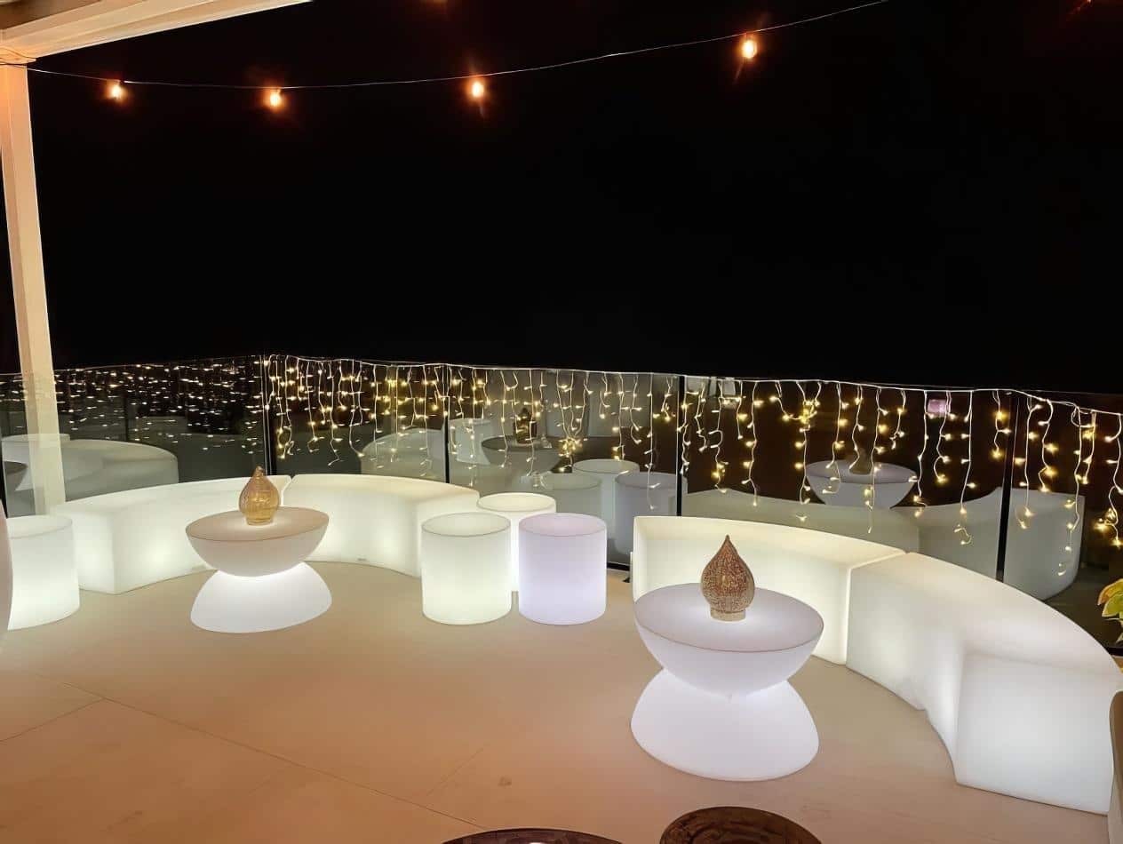 A balcony bar with white glowing lights and stools for hire.