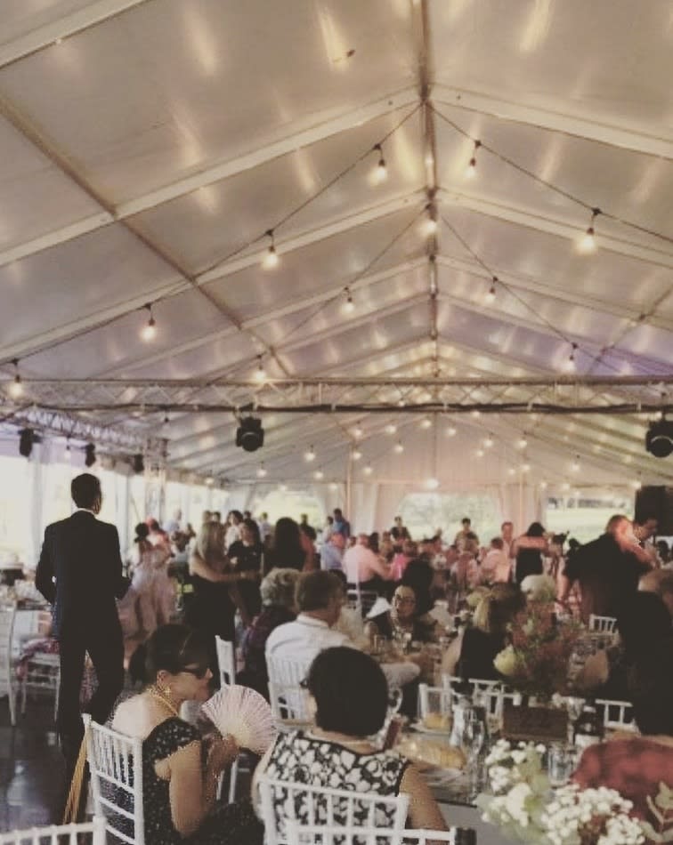 A group of people sitting at tables in a tent adorned with Festoon Light Hire.