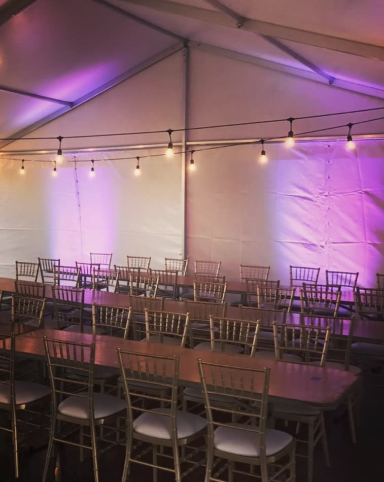 A tent with tables and chairs set up with purple festoon lighting.