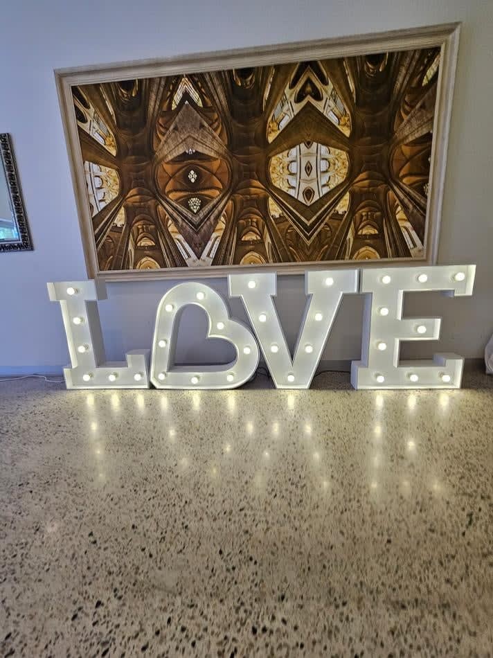 A large light up "LOVE" sign in front of a painting.