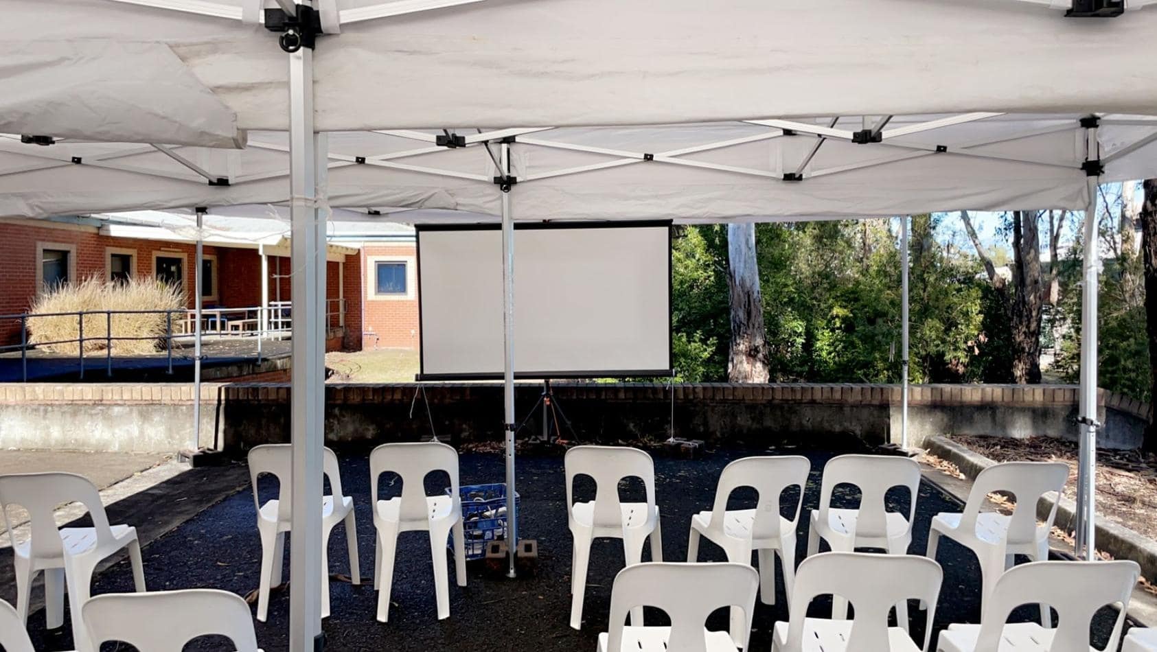 A white tent with white chairs and a projector screen hire.