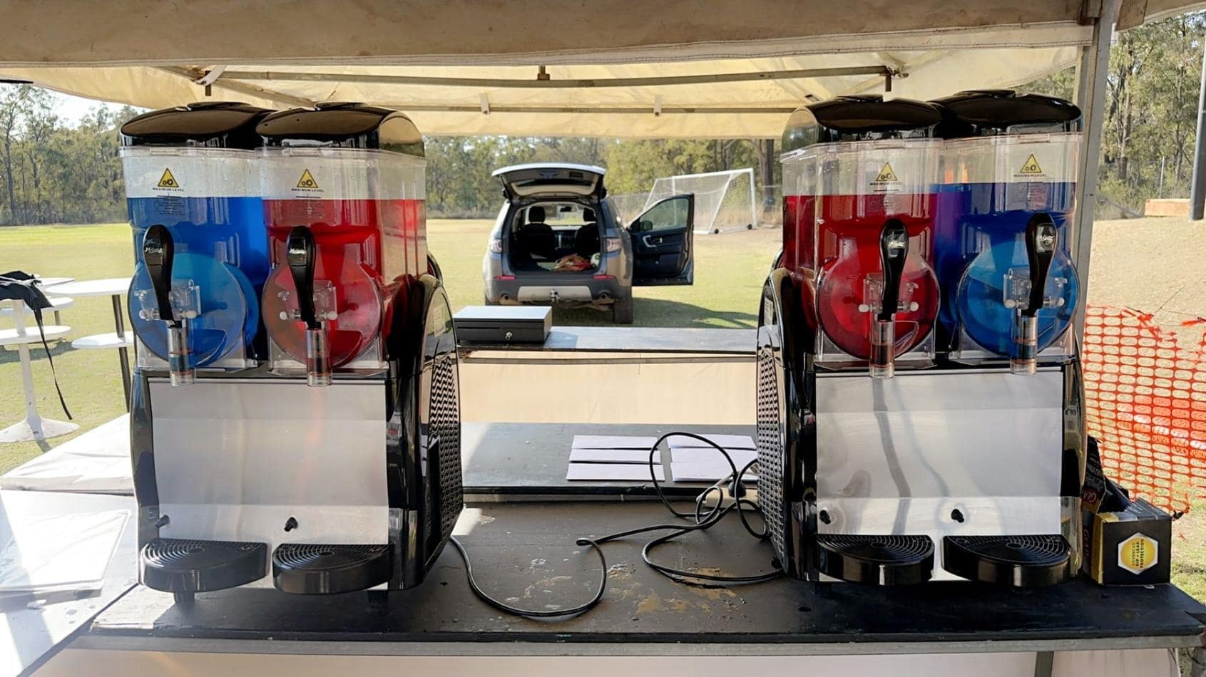 Two slushie machines are sitting on a table in front of a tent.