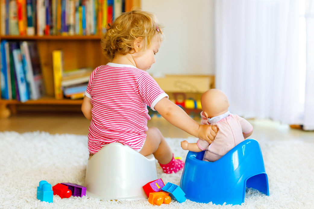 A young toddler pretending to teach her baby to toilet train