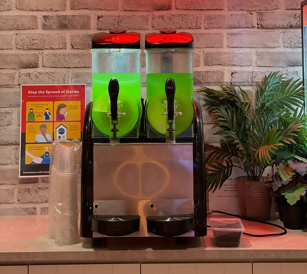 A slushie machine on a bench under a neon sign