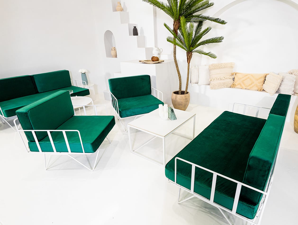 A white wire armchair lounge with green velvet cushions