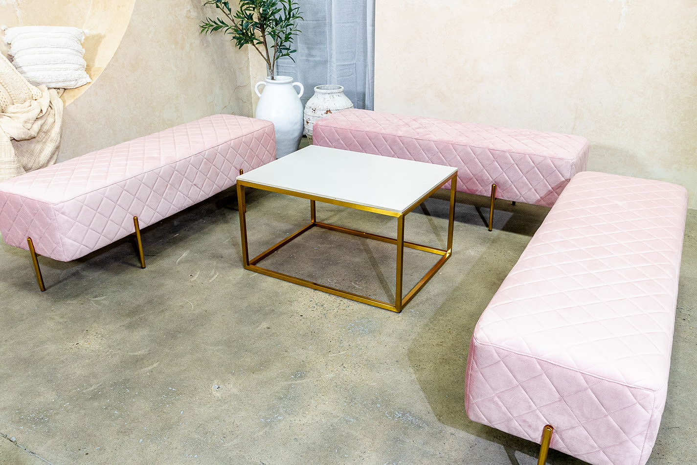 Three pink velvet ottoman benches with a coffee table in the middle