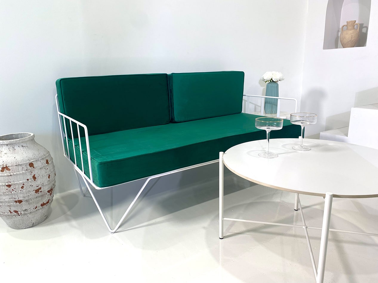 Wire sofa lounge with green velvet cushions behind a coffee table