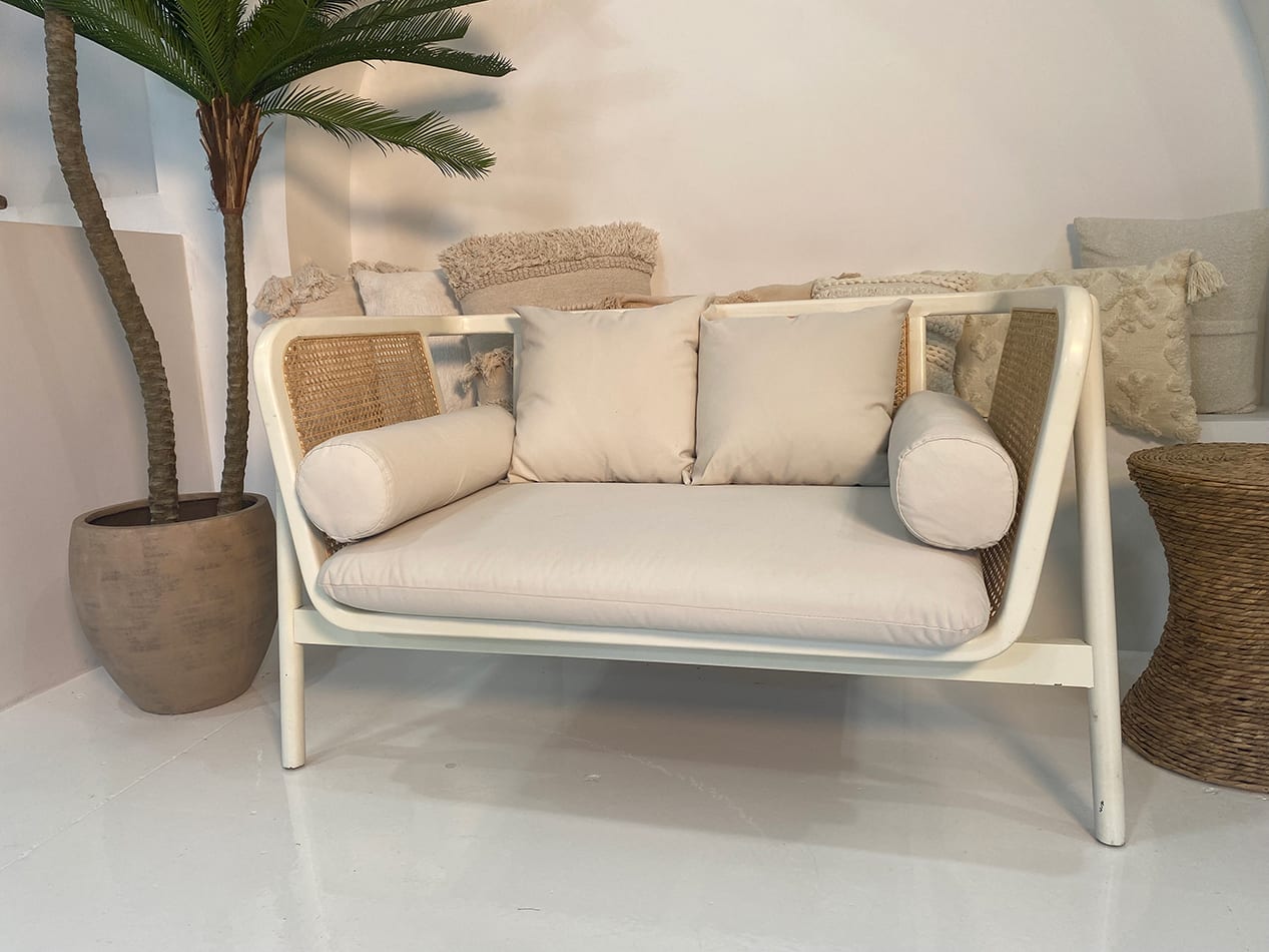 A white rattan sofa lounge next to a palm tree