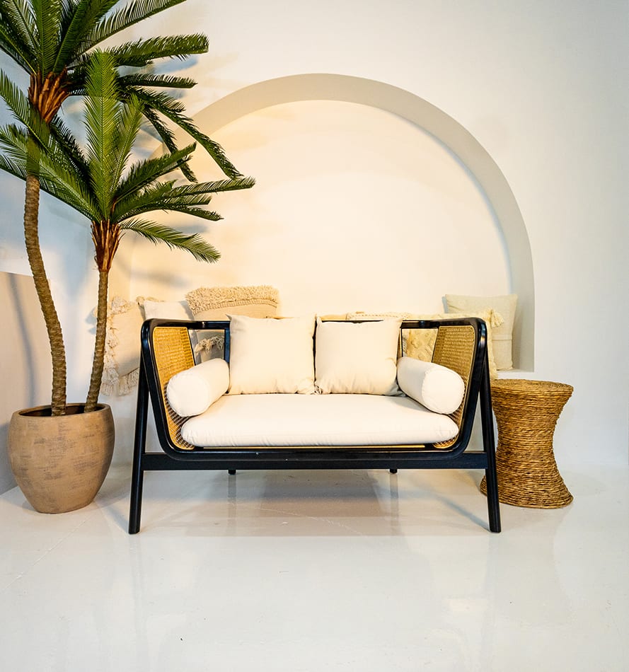 A black rattan sofa lounge set up next to a palm tree