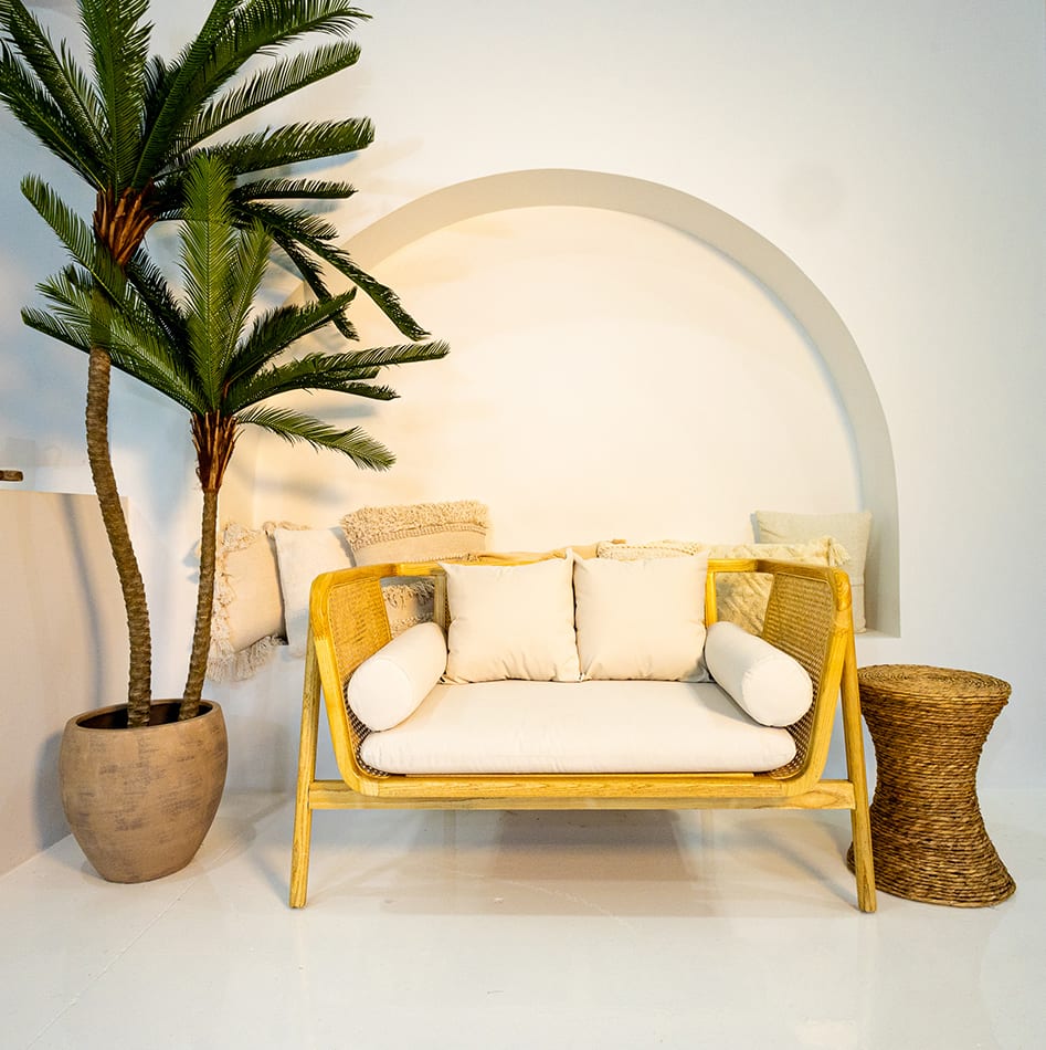 A natural coloured rattan sofa lounge set next to a palm tree