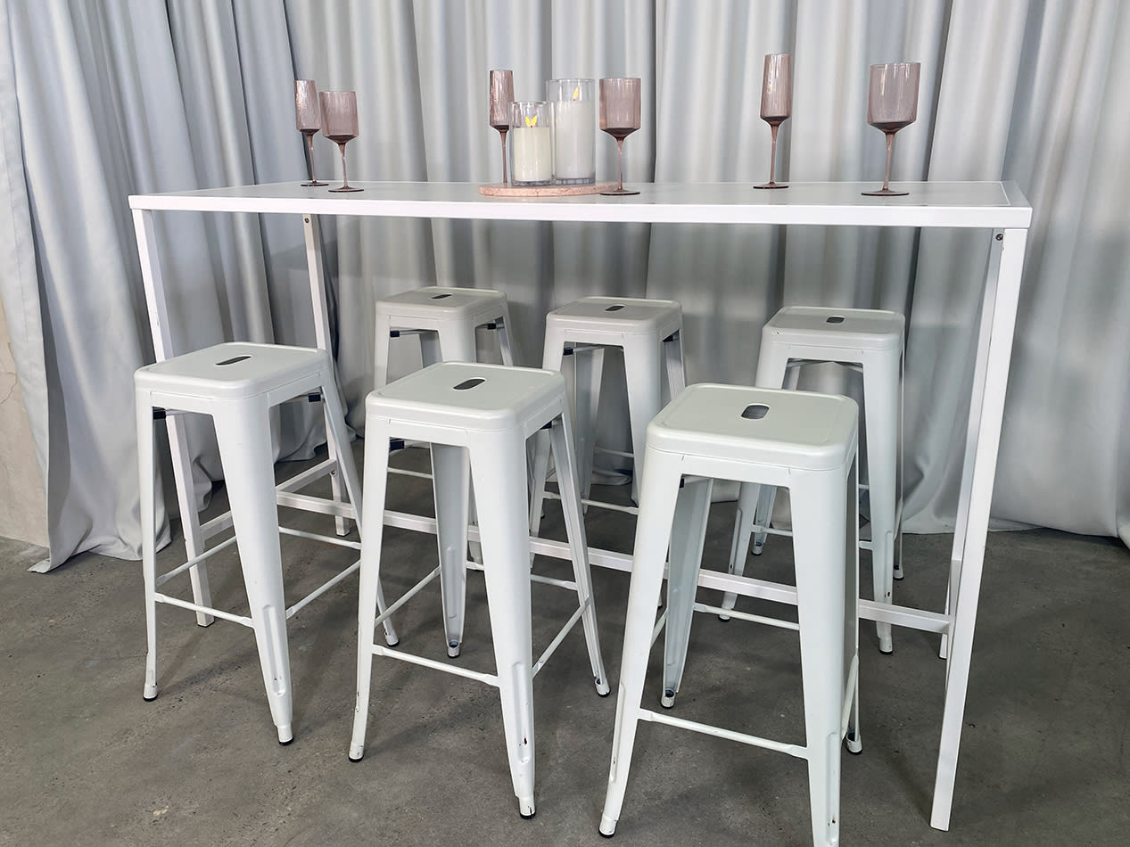 A white rectangular tapas table with stools underneath it