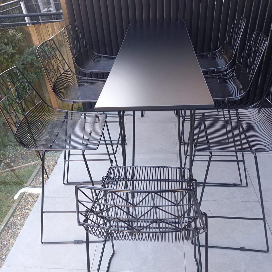 Hairpin high bar table with black top set up with wire chairs on a balcony