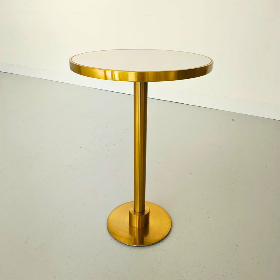 Modern round gold cocktail table with a sleek pedestal base and white tabletop, styled against a neutral background.