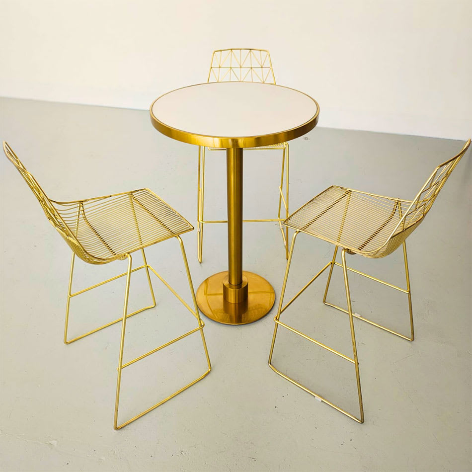 Stylish gold cocktail table with white top, paired with matching gold wire chairs in a contemporary setting.