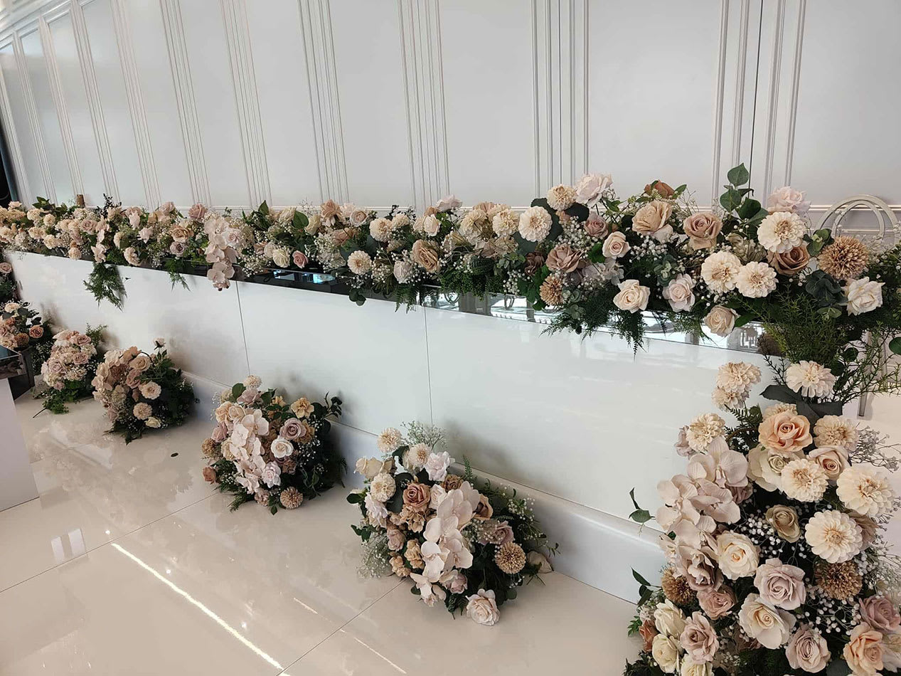 White gloss bridal table featuring elegant floral décor in soft neutral tones, with roses, orchids, and greenery styled for a modern wedding reception.