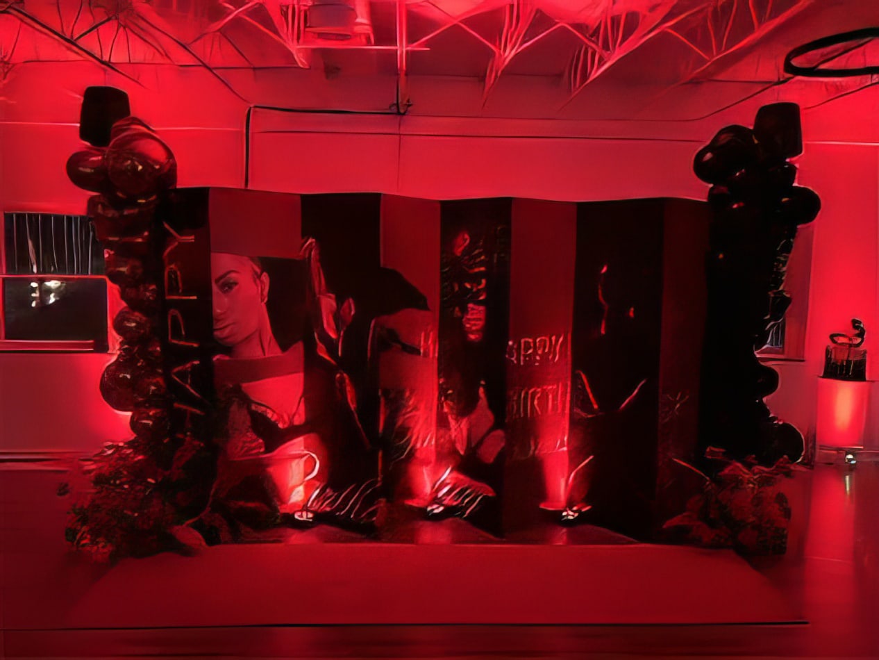 Red battery-operated par can uplights casting dramatic lighting across a custom photo backdrop with balloon décor at an indoor event.