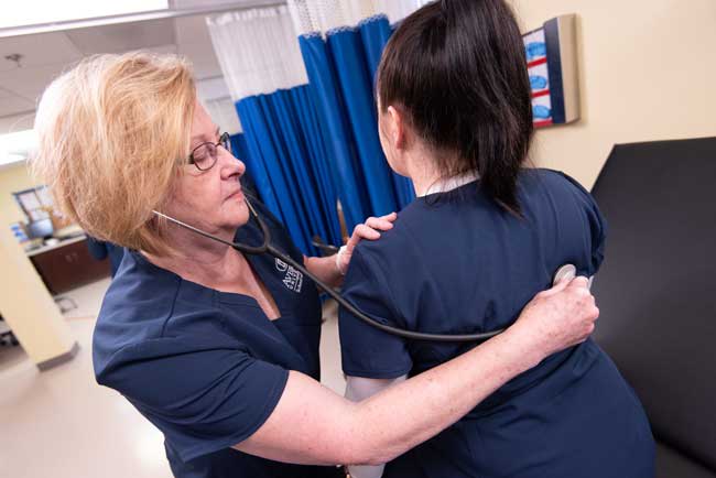 Averett nursing student listening to another nursing student's breathing