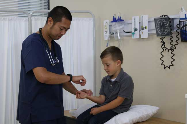 Male nurse in blue scrubs taking the pulse of a pediatric patient