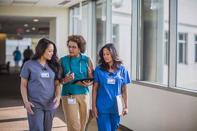 Three nurses walking and talking together down a hallway