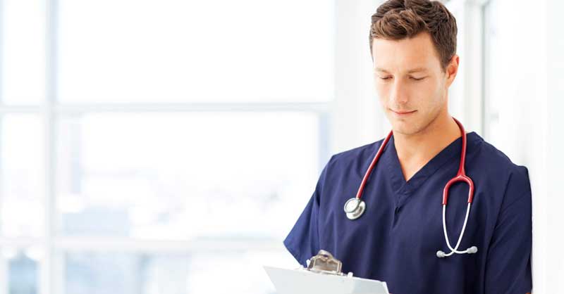 Male nurse in blue scrubs looking at clipboard