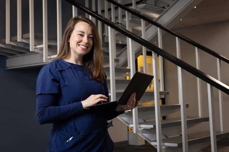 Averett ABSN student standing by stairs holding laptop