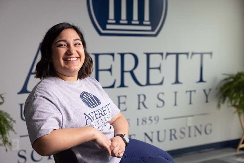 ABSN student sitting in front of University wall sign