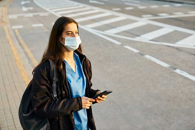 nurse standing by the side of the road, holding her phone