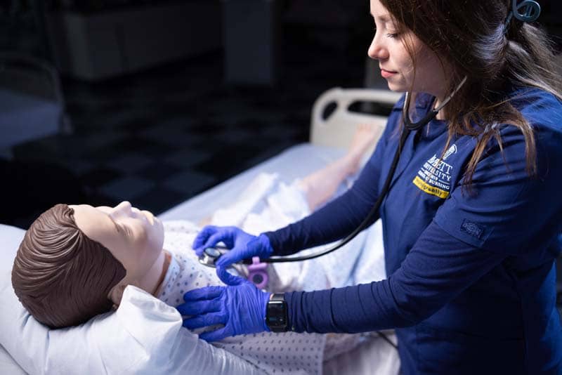 closeup of ABSN student using stethoscope on sim manikin